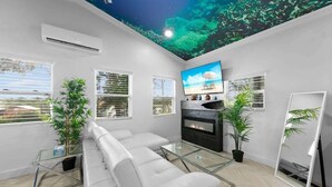 Un salon moderne comprenant un canapé, une table basse en verre, un téléviseur à écran plat, une cheminée et une fresque murale au plafond.