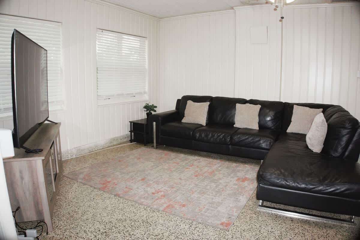 A living room with a black leather sofa, a television on a stand, and a patterned rug.