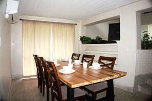 A dining area with a wooden table set for six, surrounded by chairs, with a window and curtains in the background. - Affordable, Spacious, Family Friendly, 3 Queen Beds, Washer and Dryer, Long-Term Welcome (Jacksonville)