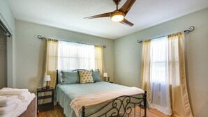 Un dormitorio con cama, mesitas de noche, ventilador de techo y cortinas.