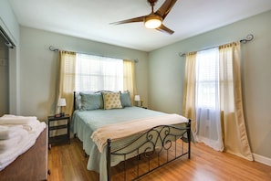 Une chambre à coucher avec un lit, des tables de chevet, un ventilateur de plafond et des rideaux.