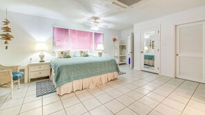 Une chambre à coucher comprenant un lit, des tables de chevet, une chaise, une fenêtre avec des stores, un ventilateur de plafond et une armoire.