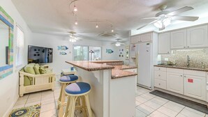 Une cuisine dotée d’un plan de travail en granit, de meubles blancs, d’un ventilateur de plafond et d’un réfrigérateur.