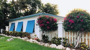 Une maison de plain-pied, à l’extérieur blanc et aux volets bleus, entourée d’une pelouse bien entretenue et de plantes en fleurs.