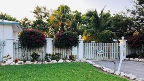 A gated property with a white fence, a mailbox, and lush greenery including palm trees and flowering plants. - Lush tropical plantings in a gated compound located directly on the Florida Bay (Islamorada)