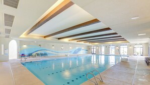 An indoor swimming pool with clear lane markings, a lifeguard chair, and a seating area with tables and chairs. - Resort Pools + More Perks! 55 + Goodyear Escape (Goodyear)