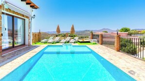 Une piscine avec des chaises longues, une terrasse en pierre et une vue sur les montagnes lointaines.