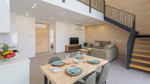 Ein zeitgemäßer Wohnraum mit Essbereich, einer Couch, einem Fernseher und einer Treppe.