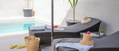 A poolside lounge area with wicker furniture, a pool, and potted plants.