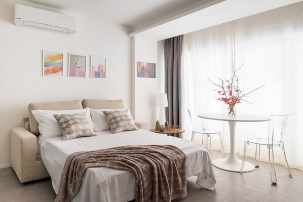 A modern bedroom with a bed, bedside table, and a round dining table with chairs.
