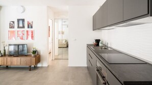 A modern kitchen with dark cabinets, a black countertop, and a built-in oven. There is a wooden sideboard with a flat-screen TV and decorative items. - UR-NEST San Gervasio, charming one-bedroom apartment (Bologna)