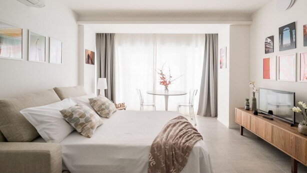 A hotel room with a bed, a TV, a small table with chairs, and a view through a window. - UR-NEST San Gervasio, charming one-bedroom apartment (Bologna)