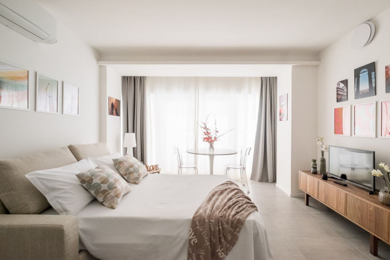 A hotel room with a bed, a TV, a small table with chairs, and a view through a window.