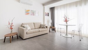 A modern living room with a beige sofa, a round dining table with chairs, a small side table, and a vase with branches. - UR-NEST San Gervasio, charming one-bedroom apartment (Bologna)