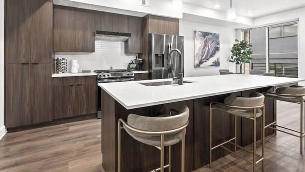 Una cucina moderna con mobili in legno scuro, un piano di lavoro bianco, elettrodomestici in acciaio inossidabile e una zona bar con sgabelli.