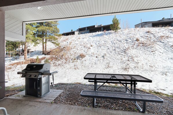 Un espacio al aire libre techado con una parrilla y una mesa de picnic, con vista a una ladera nevada.