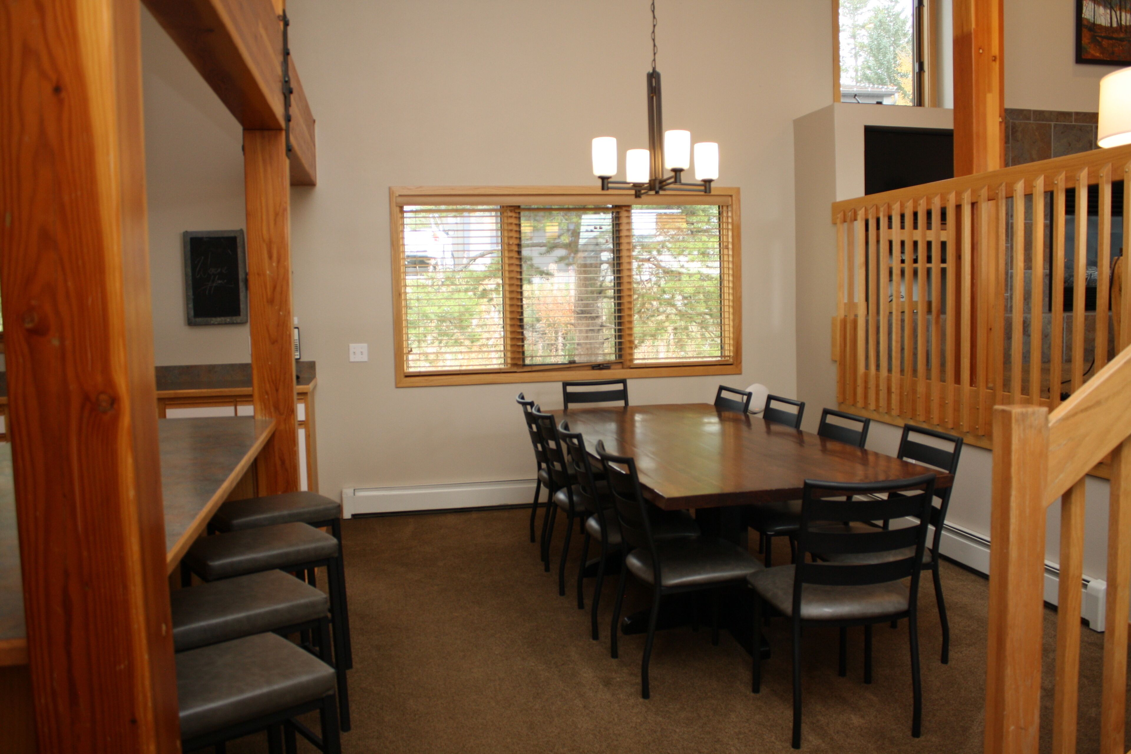 A dining area with a large wooden table surrounded by chairs, a chandelier, and a window with blinds.