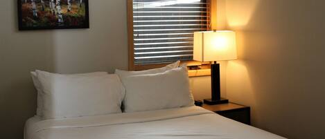 A neatly made bed with white linens, a bedside lamp, and a painting on the wall.