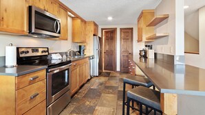 A modern kitchen with wooden cabinets, stainless steel appliances, and a stone tile floor. - Three Bedroom Townhouse. AMAZING VIEWS. On bus route. Pet friendly. (Breckenridge)