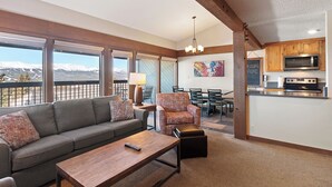 A modern living room with a sofa, armchair, and coffee table, a dining area with chairs, and a kitchen with a microwave. - Three Bedroom Townhouse. AMAZING VIEWS. On bus route. Pet friendly. (Breckenridge)