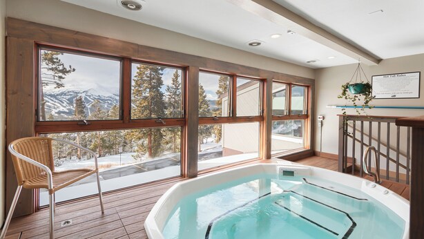 A spa area with a hot tub, wooden deck, and large windows offering mountain views. - Three Bedroom Townhouse. AMAZING VIEWS. On bus route. Pet friendly. (Breckenridge)