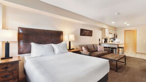 A hotel room with a large bed, a sofa, a desk, and a chair. There is a nightstand with a lamp and a dresser with drawers. - Studio Condo. AMAZING VIEWS. On bus route. Pet friendly. (Breckenridge)