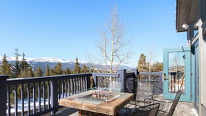 Eine Terrasse mit Feuerstelle, Tisch und Stühlen, mit Blick auf ein verschneites Gebirge.