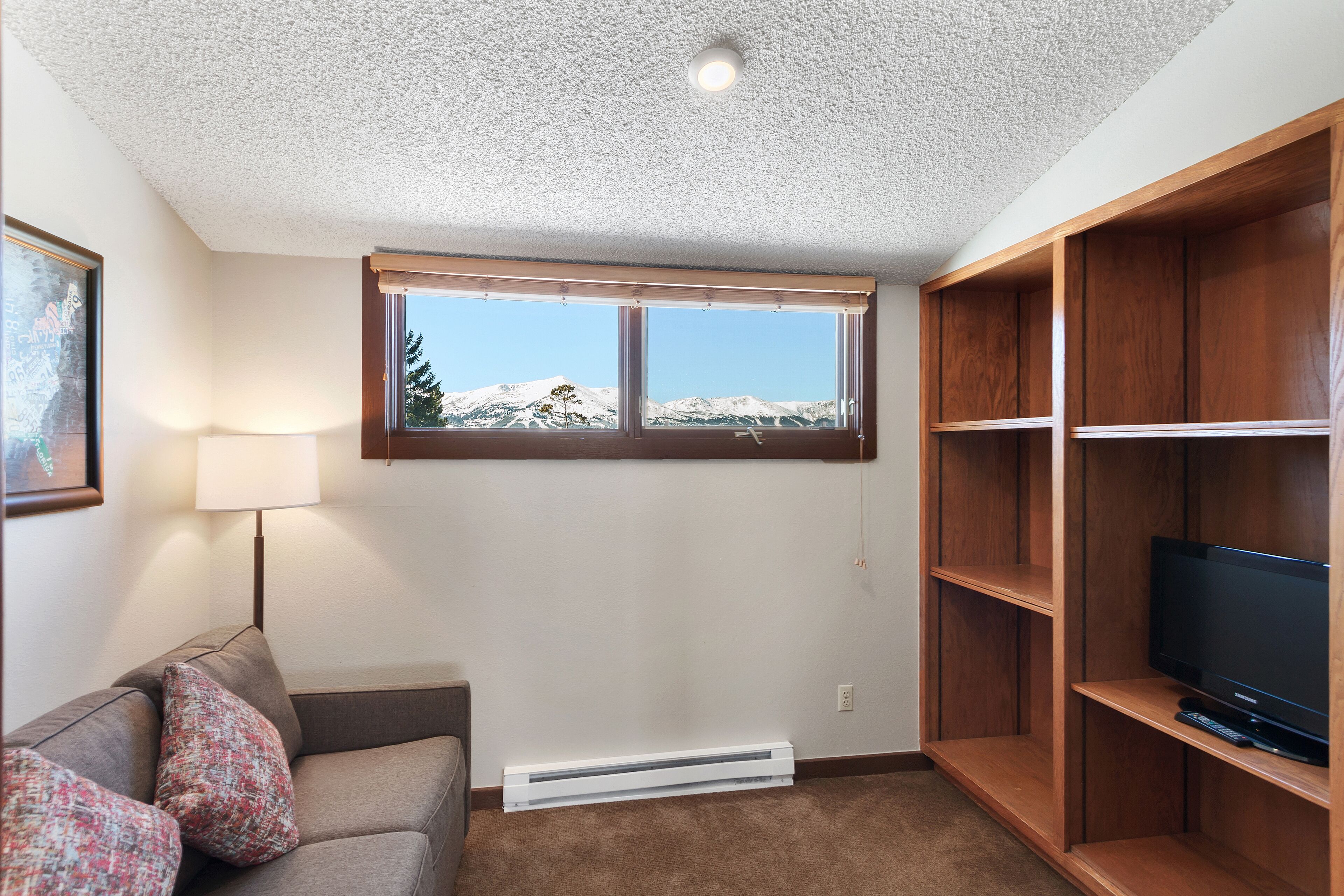 A living room with a large window, a sofa, a television, and a wooden shelving unit.