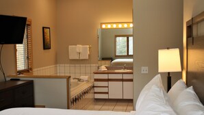 Een hotelkamer met een bed, een televisie, en een badkamer met een wastafel, spiegel en verlichting.