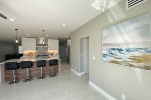 Contemporary kitchen with stove, central island, and seating area, featuring a large framed painting and modern flooring.
