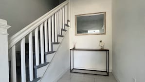 A staircase with white balusters and a black handrail, leading to a landing with a console table and a framed mirror.