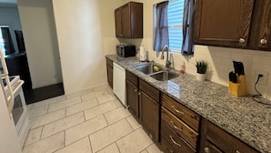 A kitchen with granite countertops, wooden cabinets, a microwave, a sink, and a window with curtains.
