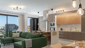 Eine moderne Wohnung mit einem grünen Sofa, Essbereich, Küche und großen Fenstern mit Blick auf die Stadt.