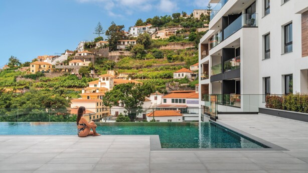 Ein modernes Hotel mit Poolbereich, Blick auf Hügelhäuser und einem klaren Himmel.