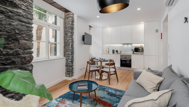 A modern living room with a stone accent wall, a dining area with a round table and chairs, and a kitchen in the background.