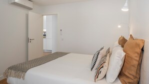 A bedroom with a bed, pillows, a blanket, a wall-mounted light, and an air conditioning unit.
