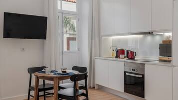 A compact kitchen with a dining area, a flat-screen TV mounted on the wall, and a window with a view of the outside.