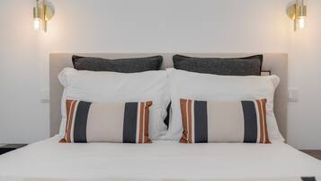 A neatly made bed with white and striped pillows, a headboard, and wall-mounted lights.