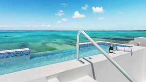 Vista de la piscina con cielo azul despejado, una botella de champán y una copa al borde.