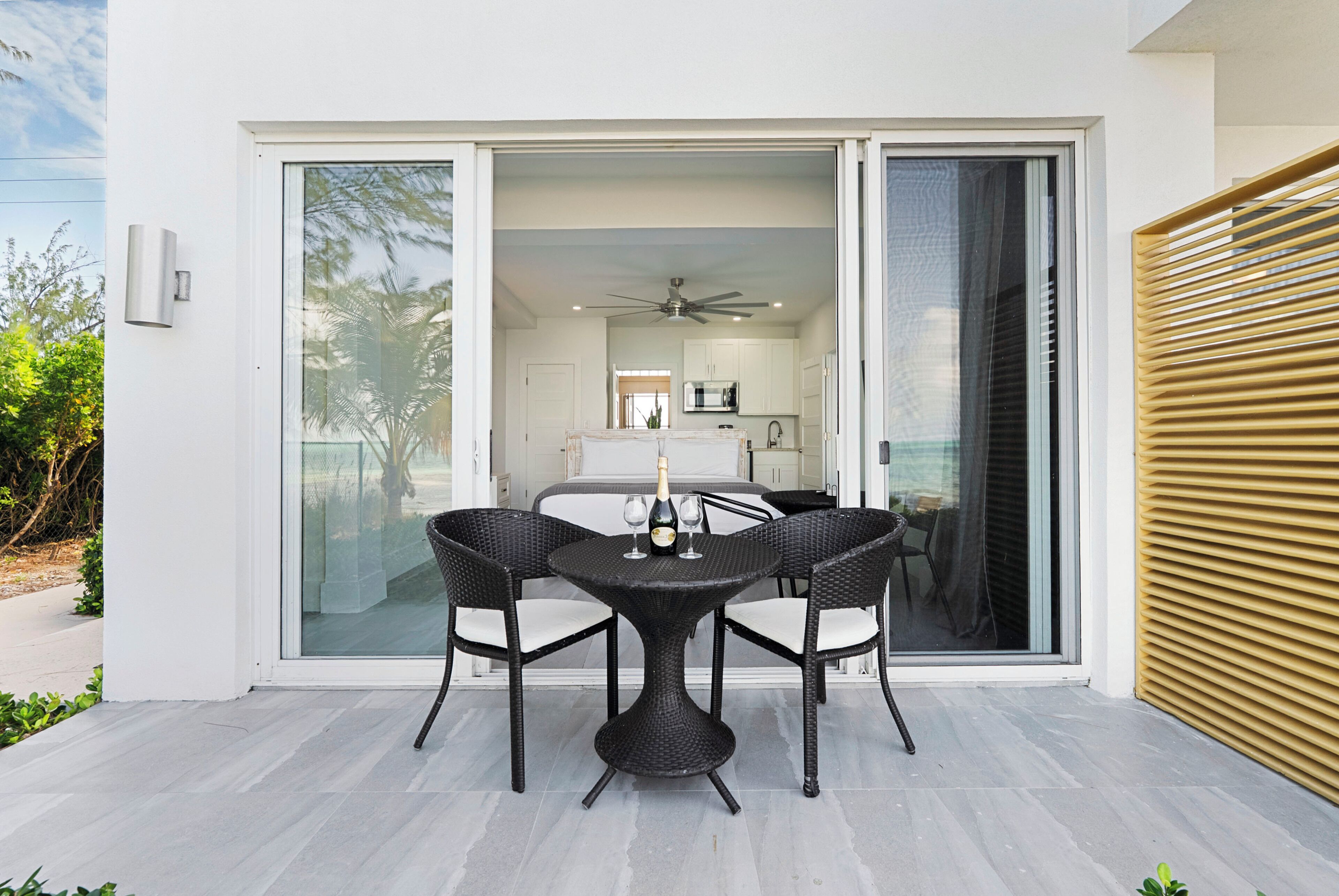 A patio with a round table and four chairs, a sliding glass door, and a ceiling fan.