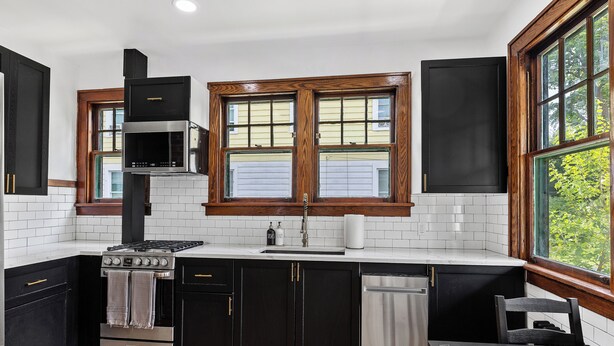 A modern kitchen with black cabinets, a stainless steel stove, and a window with a view of greenery. - Newly Renovated Gem in Melrose  - Pet Friendly (Albany)