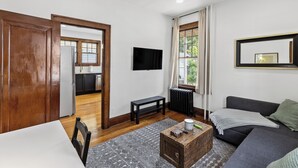 A living room with a sofa, a coffee table, a TV, and a window with curtains. - Newly Renovated Gem in Melrose  - Pet Friendly (Albany)