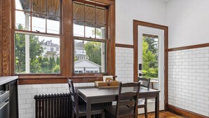 A kitchen with a wooden table and chairs, a radiator, and a window with a view of houses. - Newly Renovated Gem in Melrose  - Pet Friendly (Albany)