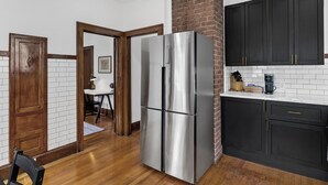 A kitchen with a stainless steel refrigerator, dark cabinets, and a brick accent wall. - Newly Renovated Gem in Melrose  - Pet Friendly (Albany)