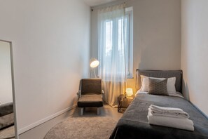A bedroom with a bed, a chair, a lamp, and a window with curtains.