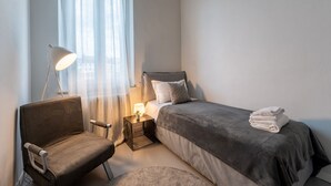 A bedroom with a bed, a chair, a nightstand, and a lamp.
