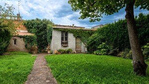 A rustic stone building with a tiled roof, surrounded by lush greenery and a stone pathway leading to the entrance.