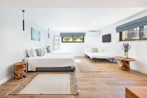 Une chambre moderne avec un grand lit, un lit plus petit, une table de chevet en bois et une grande fenêtre donnant sur un beau paysage.