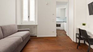 A modern apartment with a grey sofa, a dining area with a black chair, and a kitchen in the background. - GuestHost - Nice and small Studio-Milan Central Station (Milano)