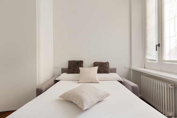 A minimalist bedroom with a bed, two pillows, a radiator, and a window.